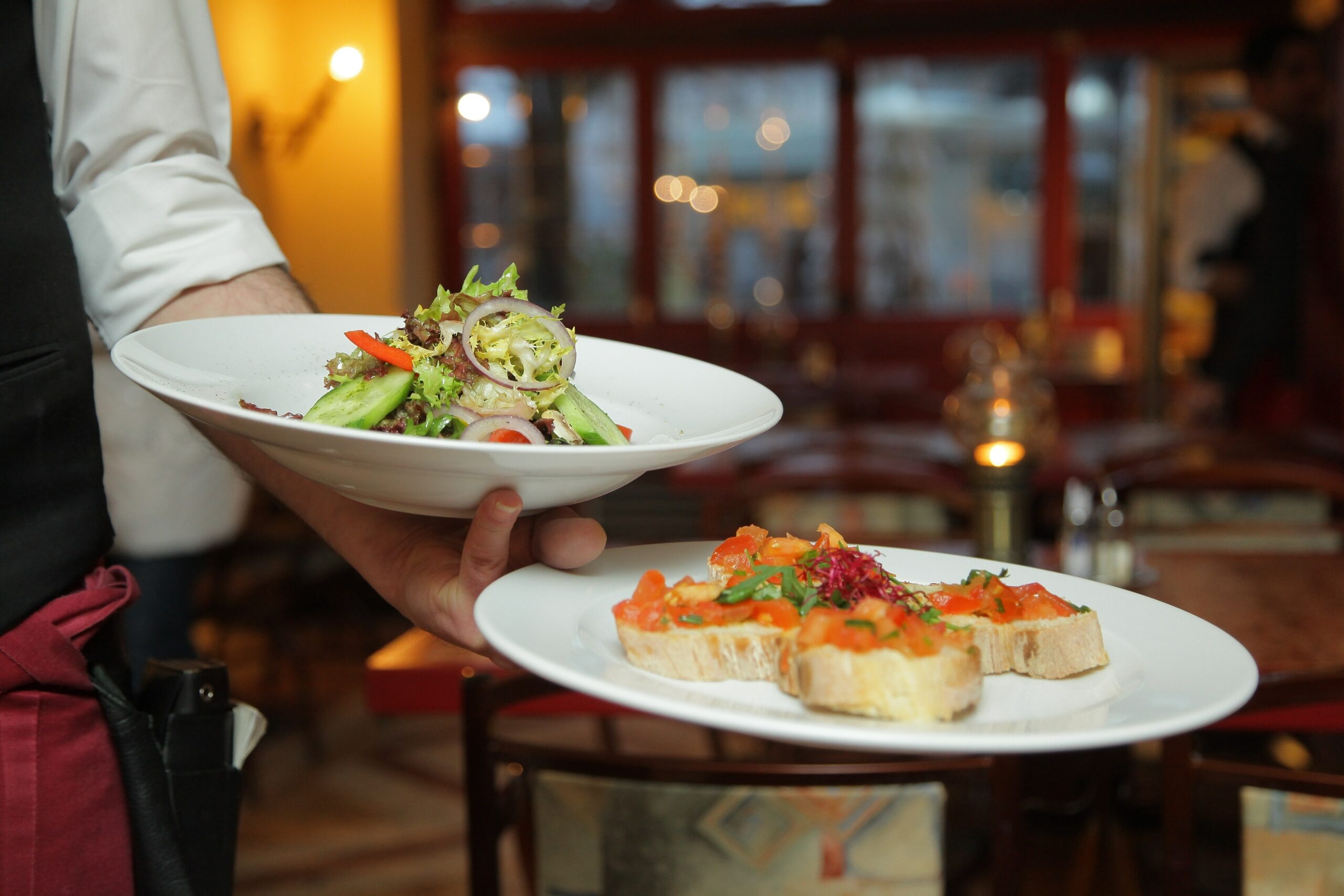 A waiter hold two plates of salad and bruschetta on his hand.