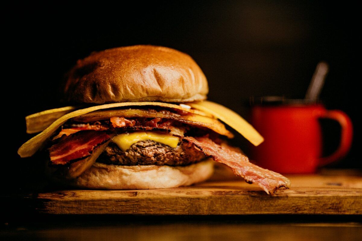 A burger is placed on the table with a red cup in the background.