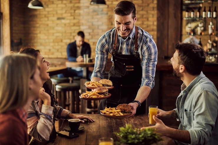 A waiter brings three burgers with French fries.