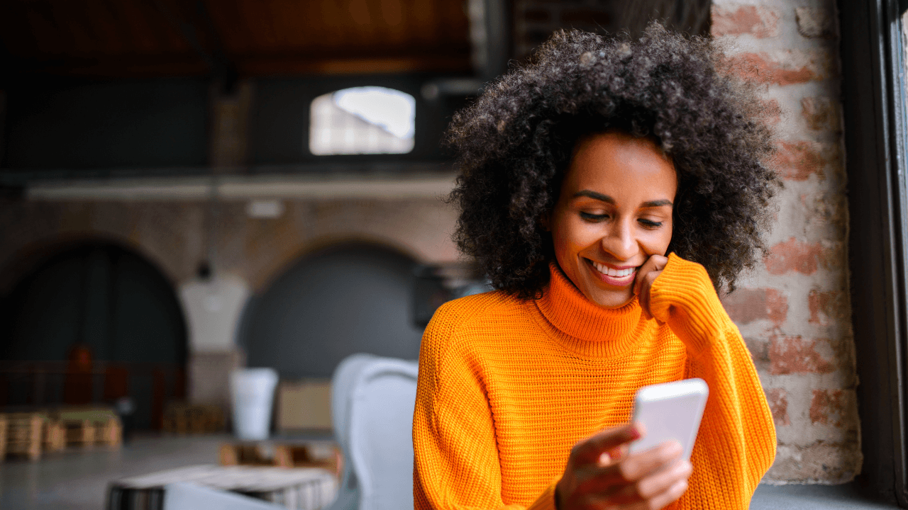 A curly-haired girl look at her smartphone smilingly.