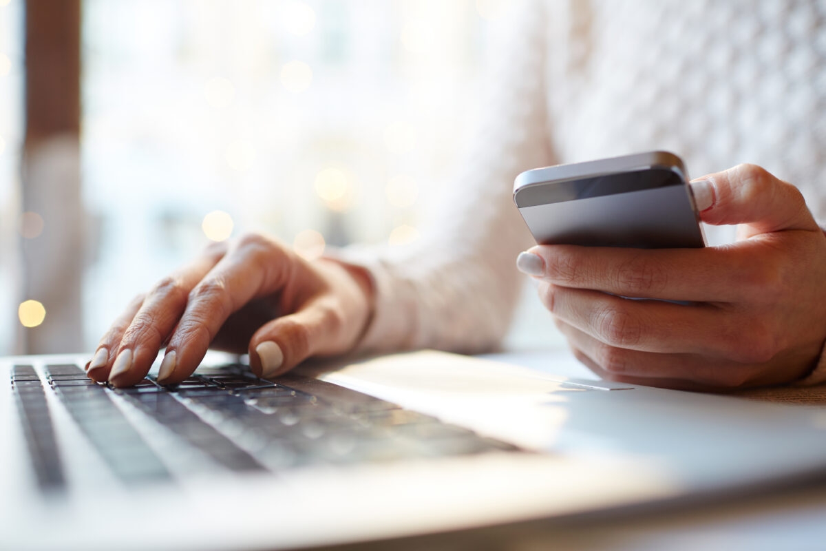 Someone holds a smartphone and works with a laptop.