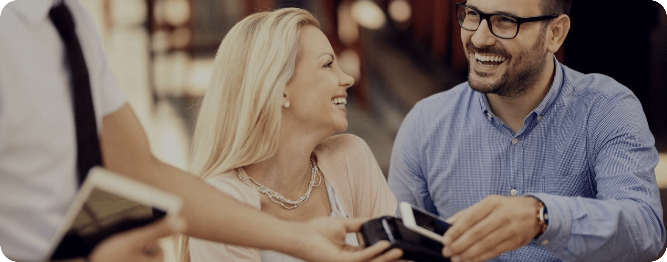 A couple pays the restaurant bill via card and smiles at the waiter.