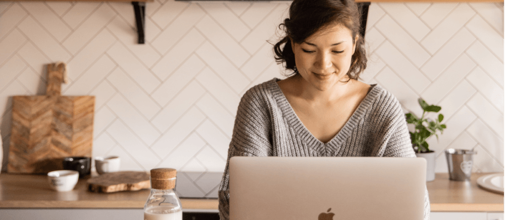 A girl is sitting in her kitchen and is working with her MacBook.