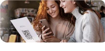 Two girls are sitting at the restaurant, one of them looks at the menu, the other one on her smartphone.