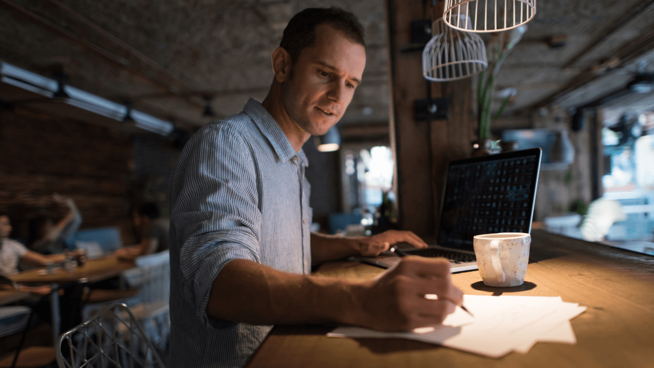 A young man works with his laptop and makes notes.