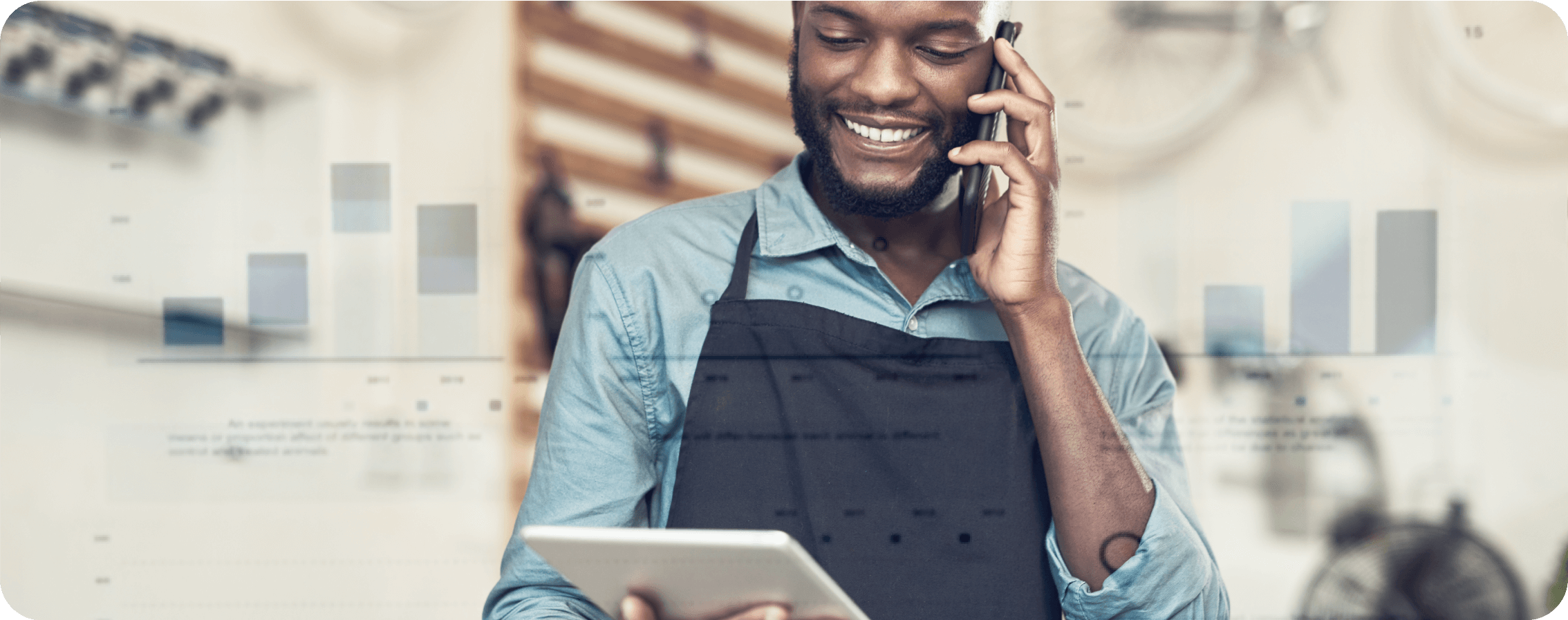 A guy is speaks with his phone and stares to his tablet smiling.