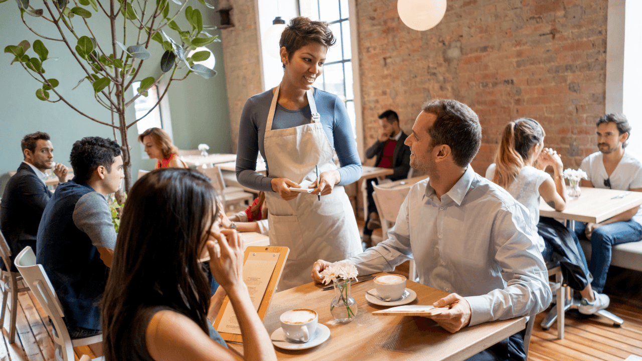 A waiter talks with a customer, sitting with a girl in a restaurant.