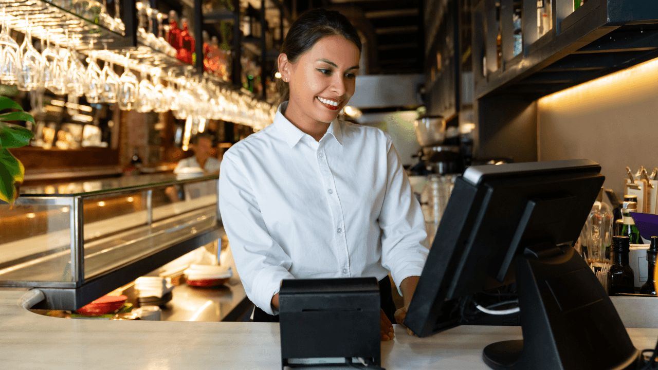 A cashier smilingly starting at the cashier monitor.