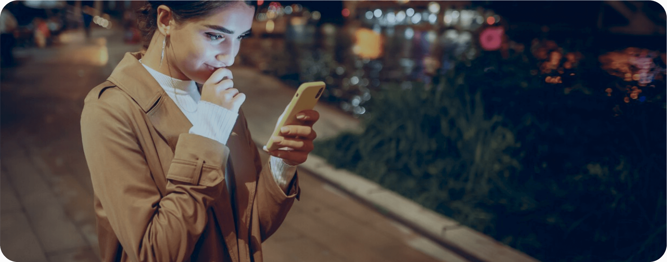 A girl is staring at her smartphone standing in the street.