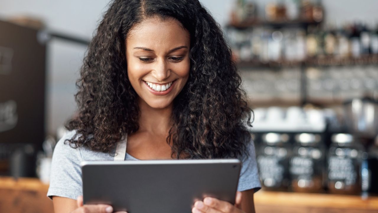 A curly-haired girl looks at her tablet smilingly.