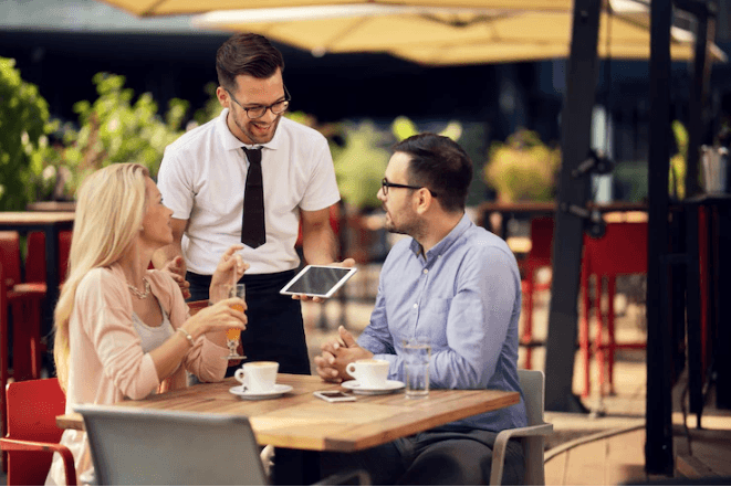 A waiter is talking with a couple in the restaurant.