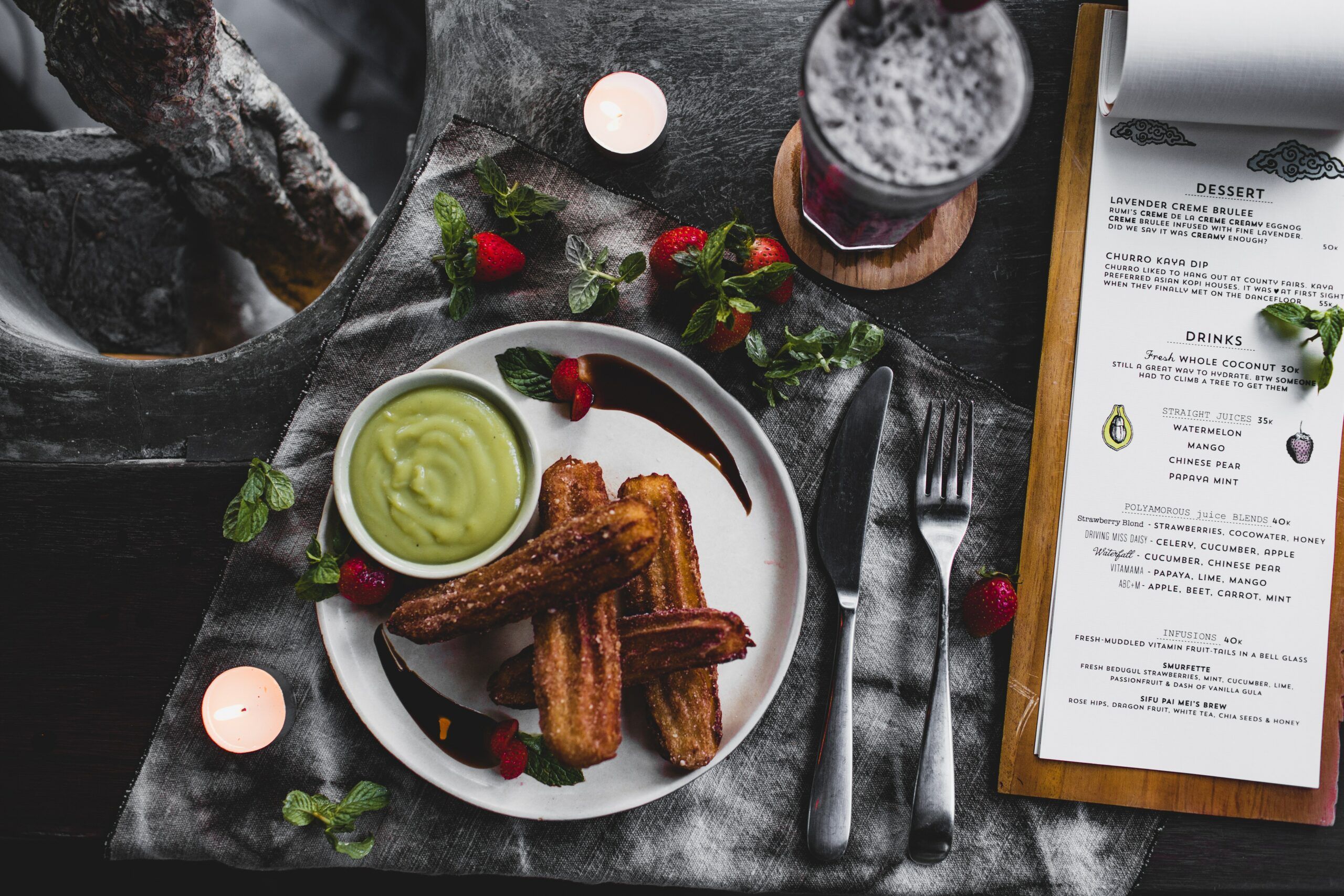 A churro with a souse placed next to a menu and cocktail.