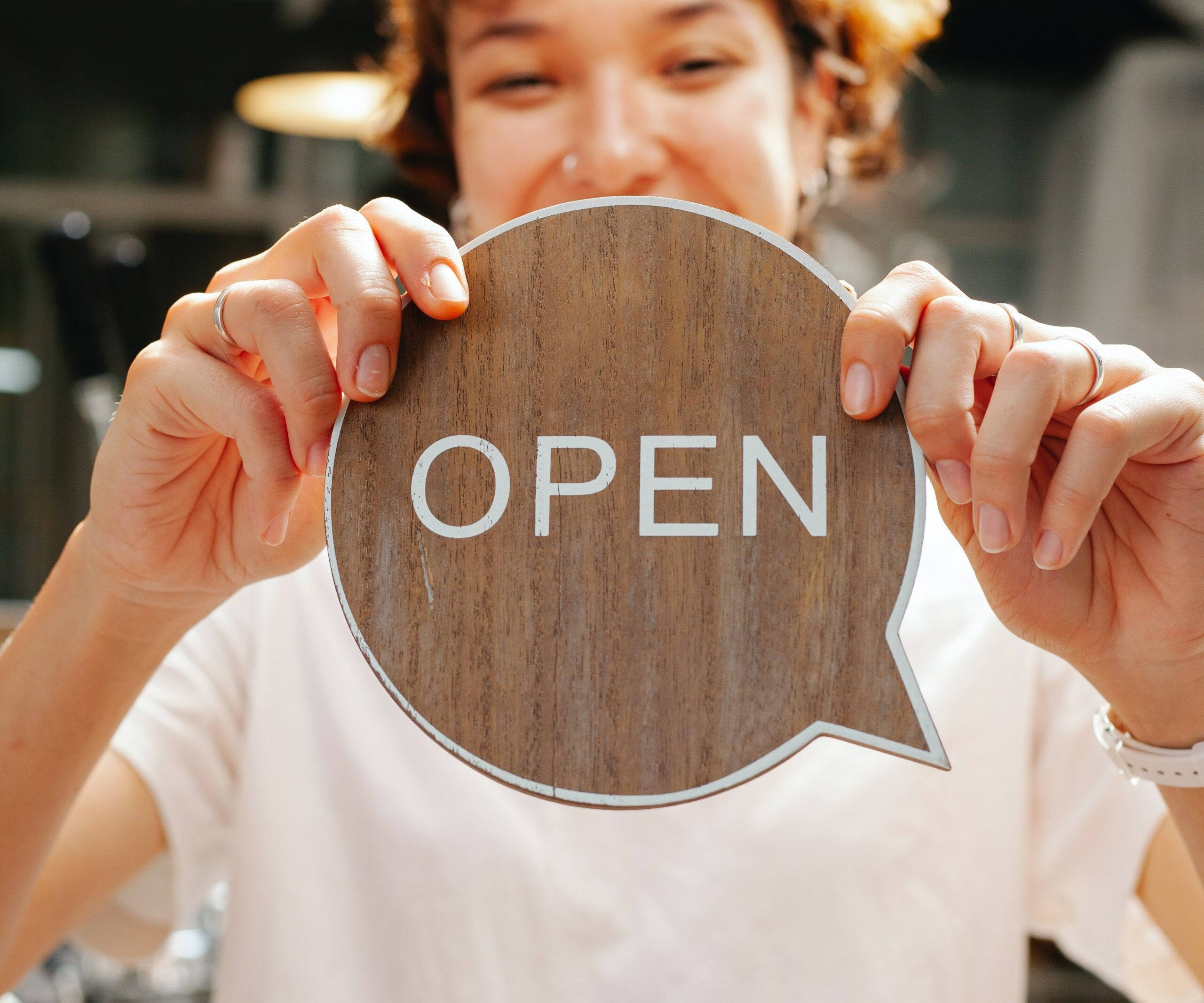 A girl is holding a wooden circle with Open written on it.