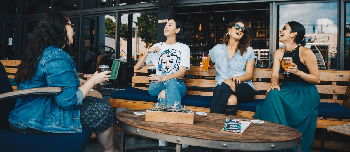 Four young ladies drink beer and laugh.