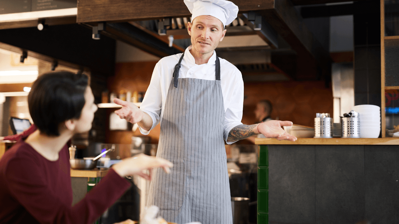 A chef in uniform conversing with a woman.