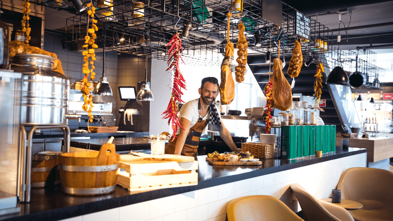 A restaurant waiter in apron is looking at the camera and smiling.