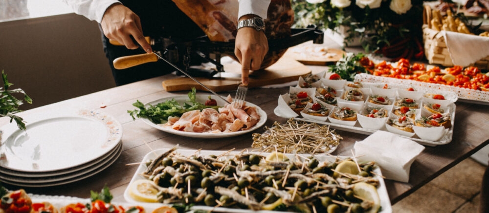 A catering set is placed on the table and a cook cuts the sausage.