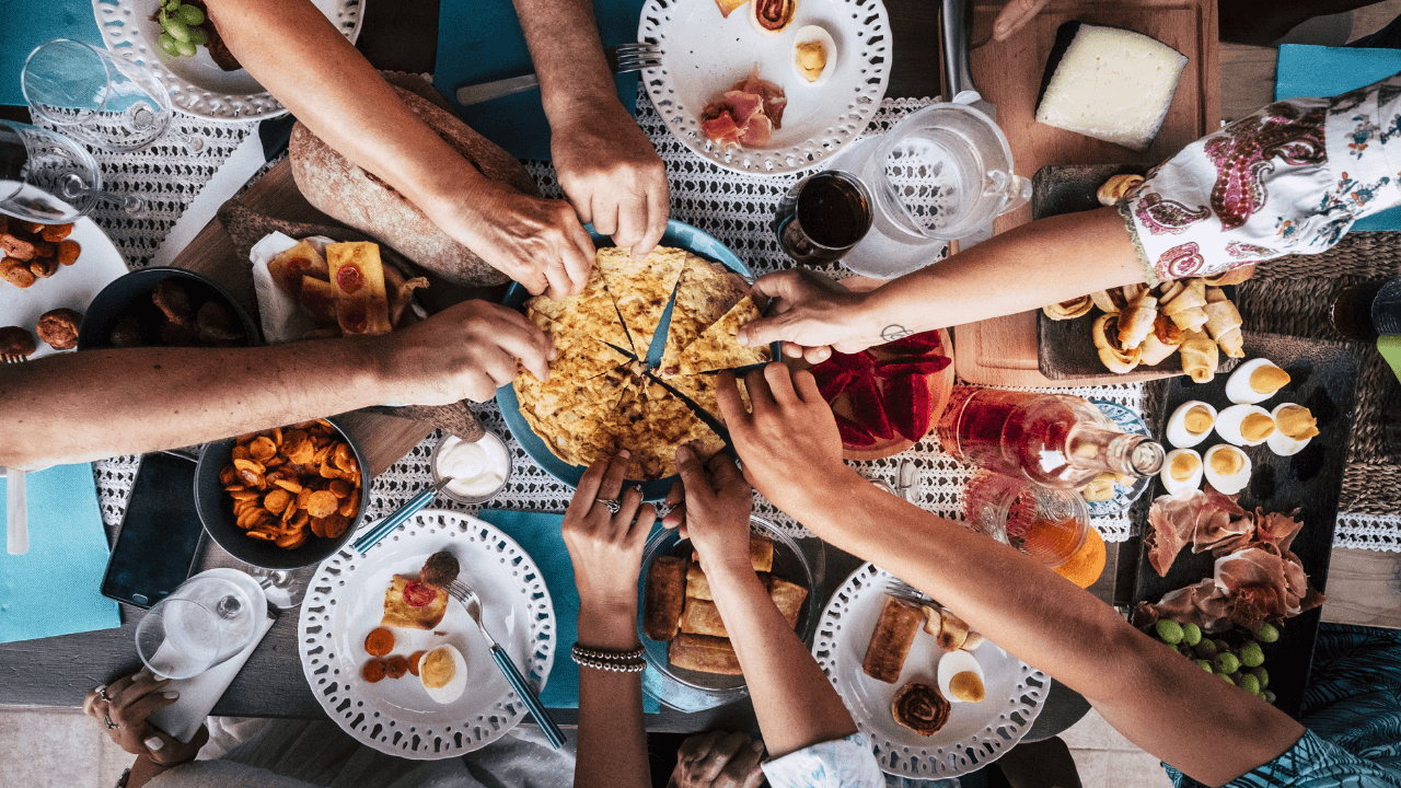 A group of people taking a piece of pizza from one plate, while having a lunch.