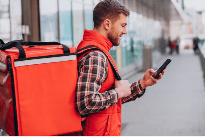 A delivery guy is looking at his smartphone.