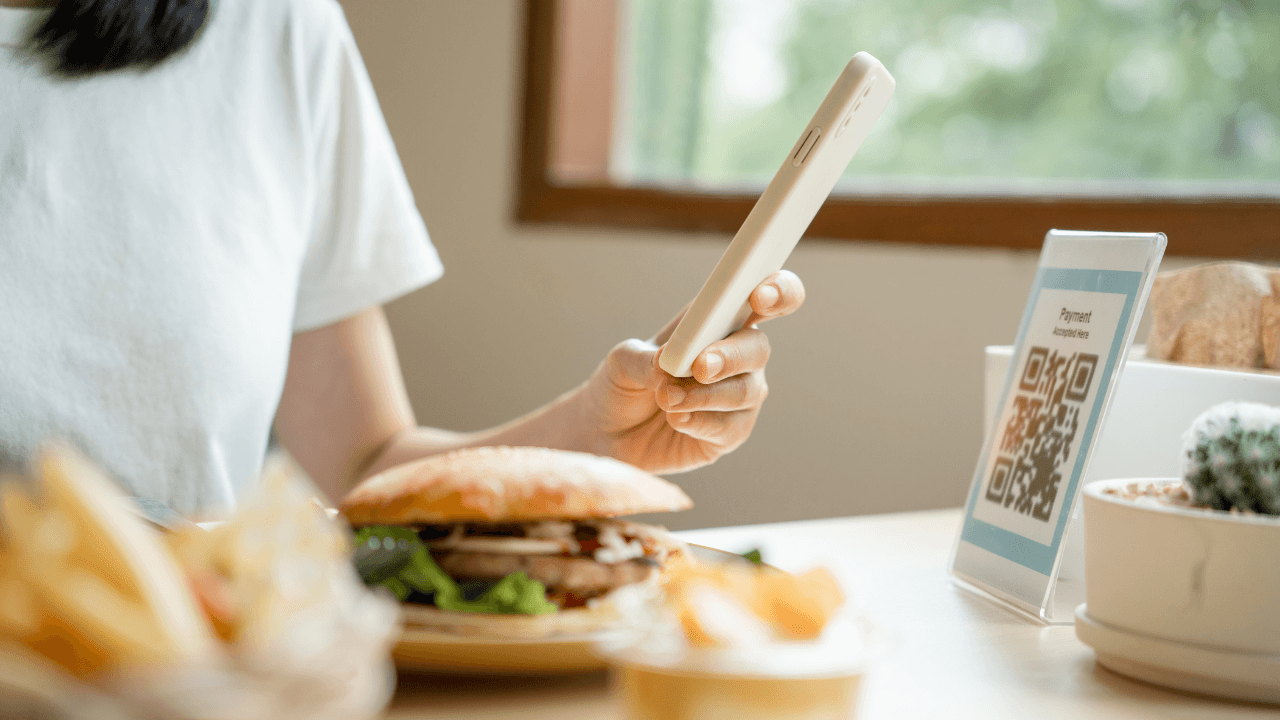 A girl is having a burger with a smartphone on her hand.