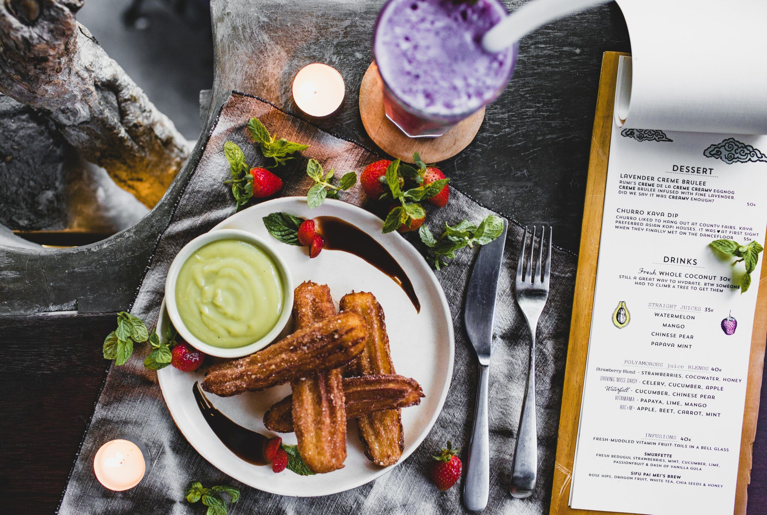 A churro with a souse and cup of cocktail is placed next to a restaurant menu.