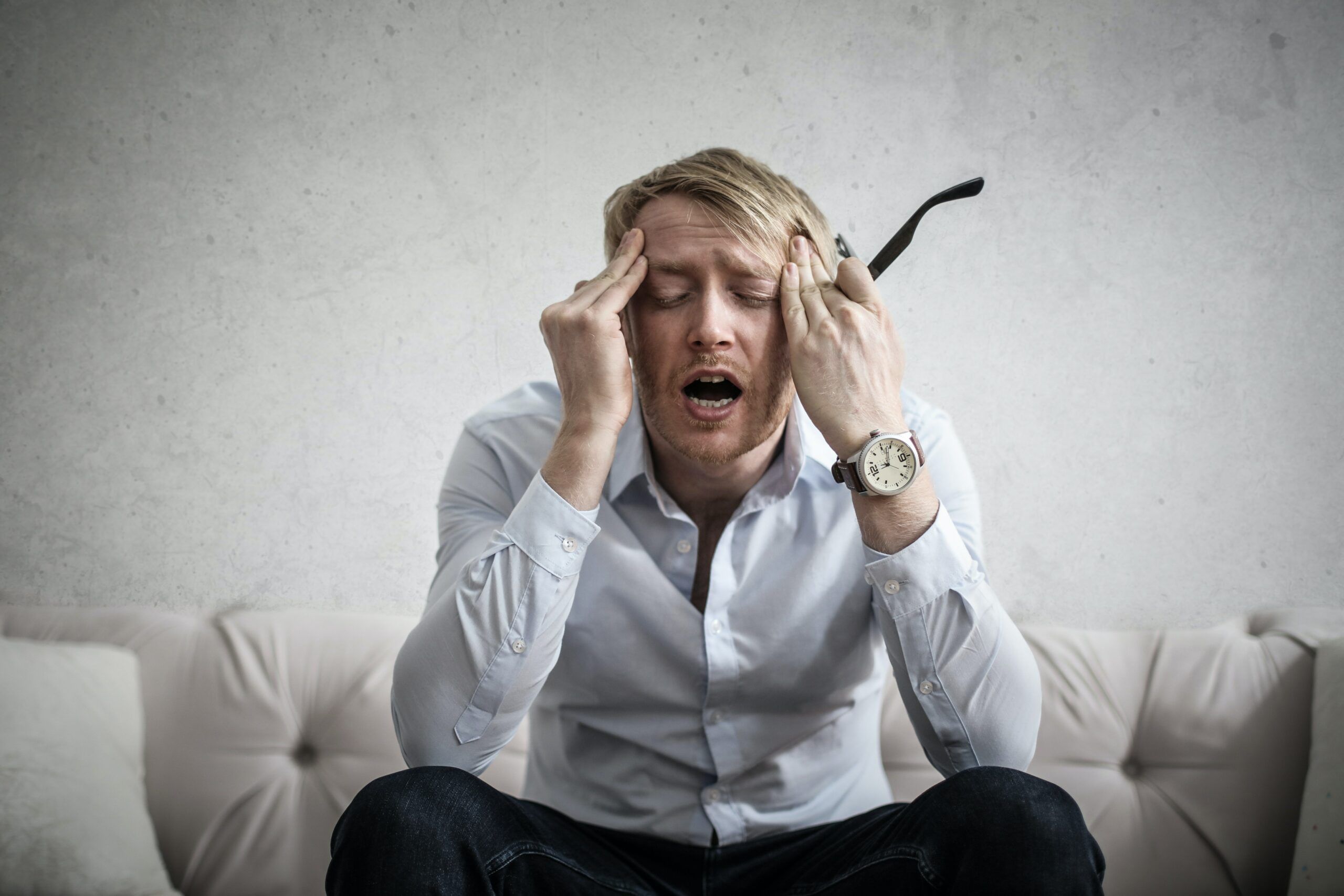 A man is sitting on the sofa with a depressive face and holds his head with his hands.