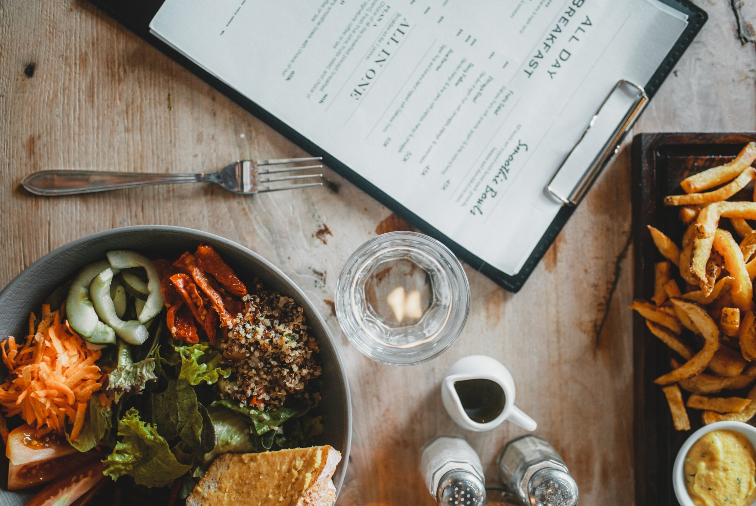 A restaurant menu is placed next to French fries and vegetable salad.