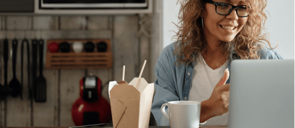 A woman is working with her laptop and eating Chinese food.