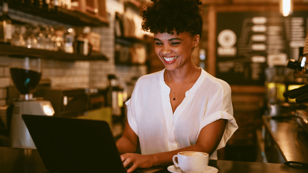 A curly-haired lady is happily lookin at her laptop.